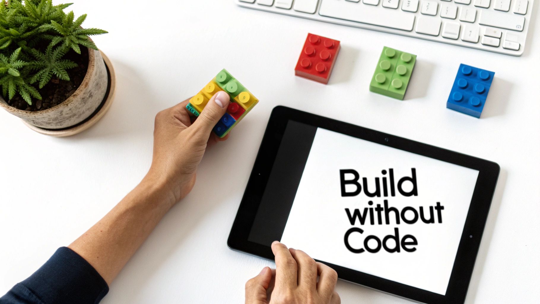 Overhead view of hands arranging colorful no-code building blocks next to a tablet displaying 'Build without Code'.